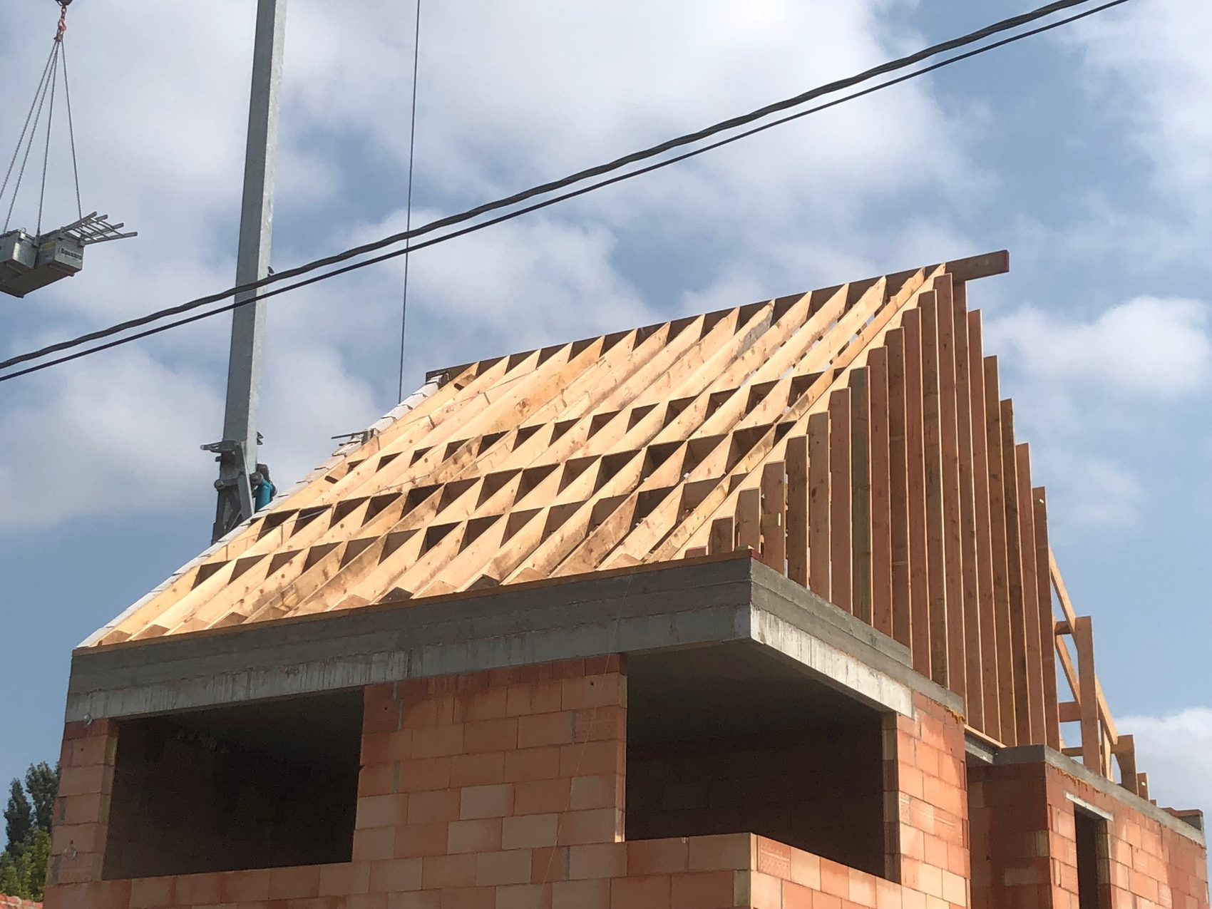 Nieuw houten dakgebinte op een woning in aanbouw, met de kraanarm nog in beeld