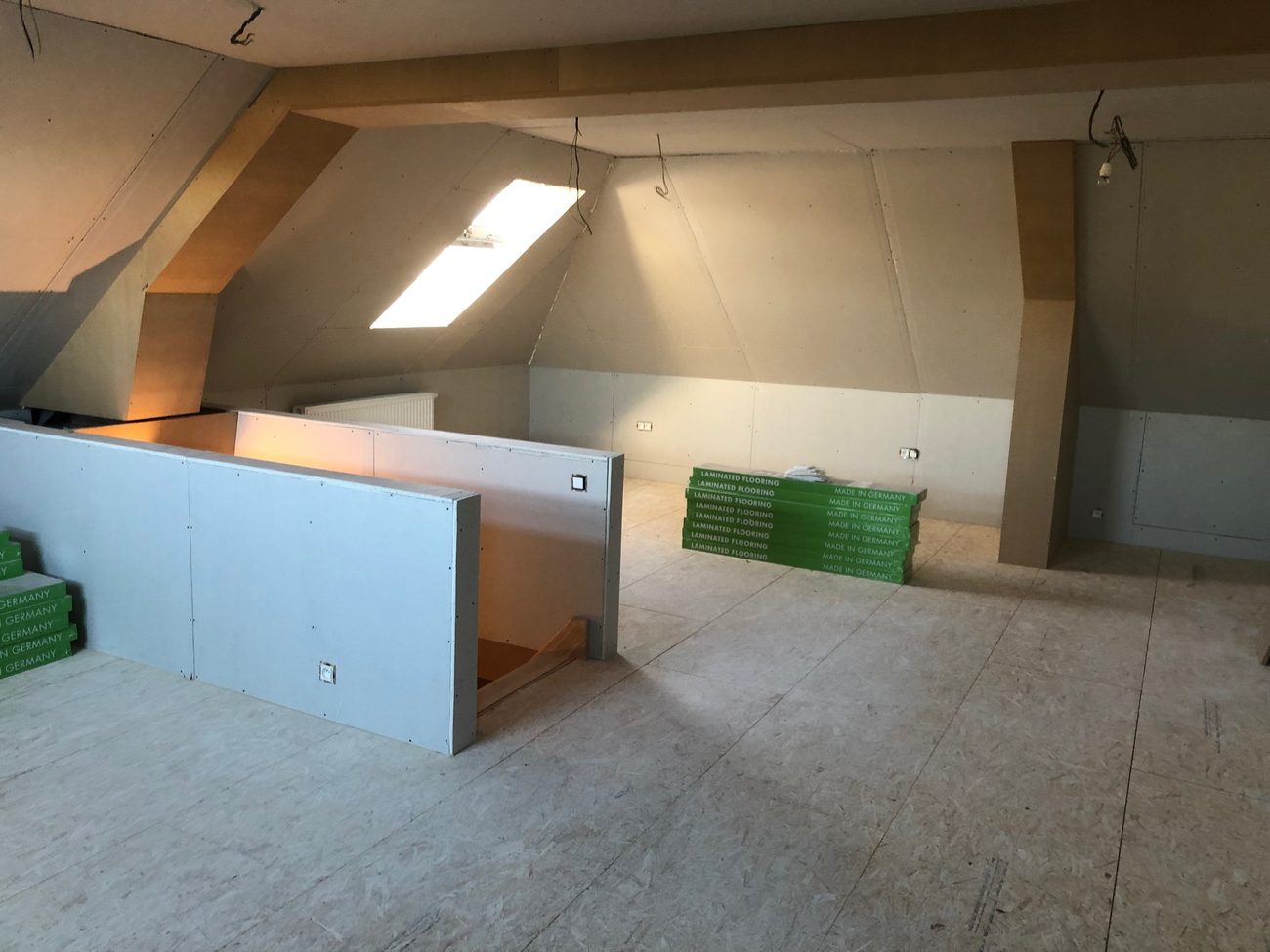Afgewerkte zolder met beplating, een dakvenster en pakken laminaat die klaarliggen op de vloer